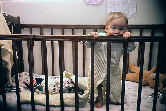 19660500 Erik 8 mos standing in crip